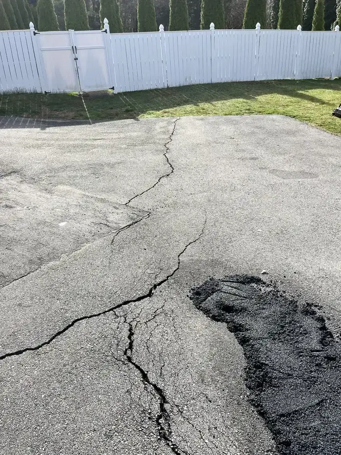 Close-up of asphalt crack showing freeze-thaw widening and edge damage requiring hot rubberized filler